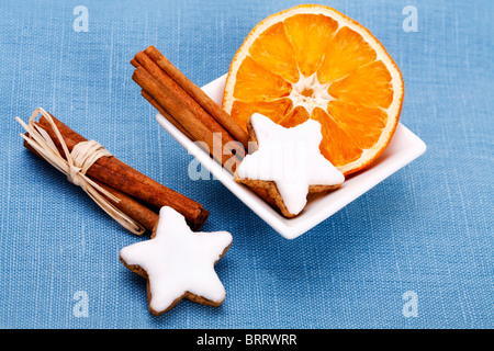 Cinnamon sticks with dried slice of orange and star-shaped cinnamon cookies in a white bowl Stock Photo