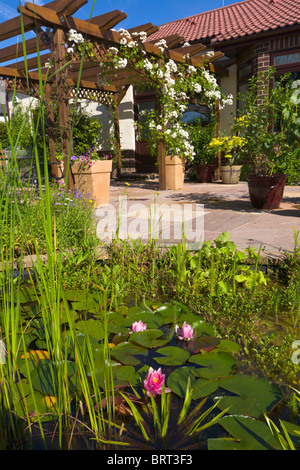 Back garden of bungalow overlooking pond with pergola and patio, England Stock Photo