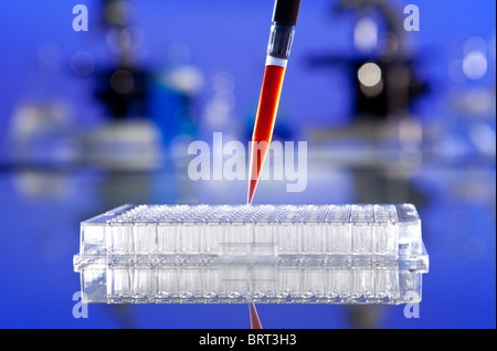 A pipette full of blood sample or red liquid and cell tray in a laboratory environment with microscopes and other equipment Stock Photo