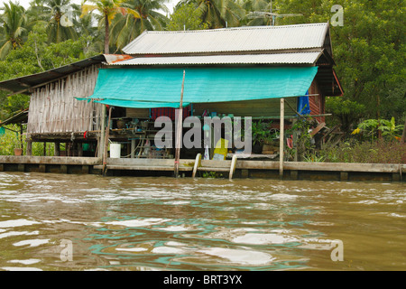 Typical Bangkok houses on stilts along khlong canal, with a small spirit house in the front.Bangkok, Thailand, September 2010 Stock Photo