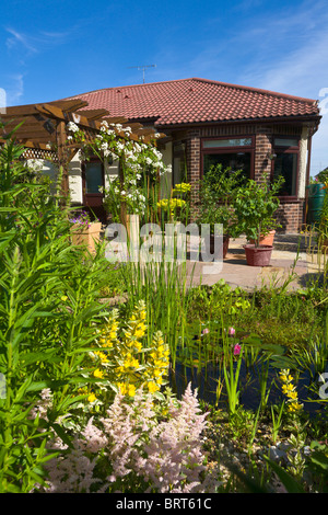 Back garden of bungalow overlooking pond with pergola and patio, England Stock Photo