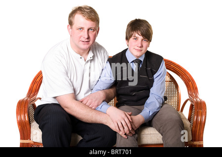 Father and son a teenage are sitting on sofa and holding hands. Isolated on white background. Studio shot. Cut out Stock Photo