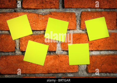 Yellow sticky notes on an old shabby red brick wall. Stock Photo