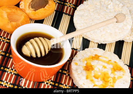 Close-up of honey in an orange pot with wooden honey dipper and apricots. Selective focus. Stock Photo