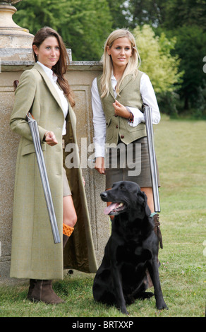 Two very attractive girls dressed for a day in the country, holding shotguns, with a  black Labrador waiting Stock Photo