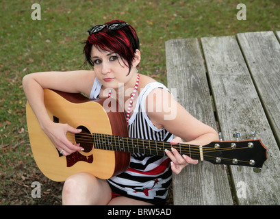 one adult woman playing guitar in a park on a picnic table Stock Photo