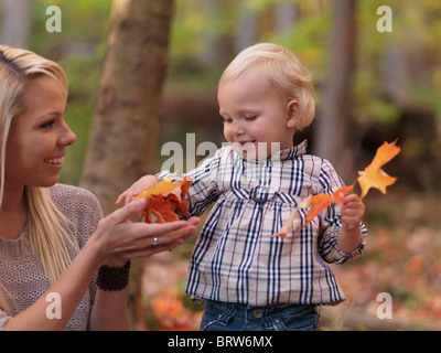 Happy two year old girl and her mother gathering fallen autumn leaves in a park Stock Photo