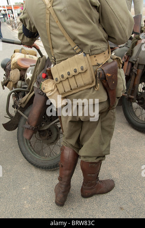 France, Normandy, Arromanches. Man in vintage US uniform, with ammo belt and gun, in front of motorcycle. Stock Photo