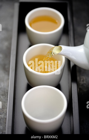 Green tea being poured from teapot into cups on tray Stock Photo