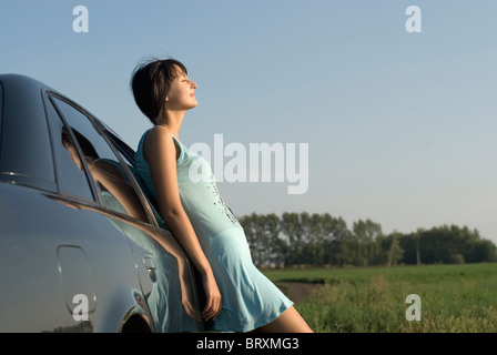 Young woman leaning to car and enjoying sunlight Stock Photo