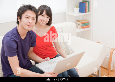 Couple using laptop on sofa, Japan Stock Photo