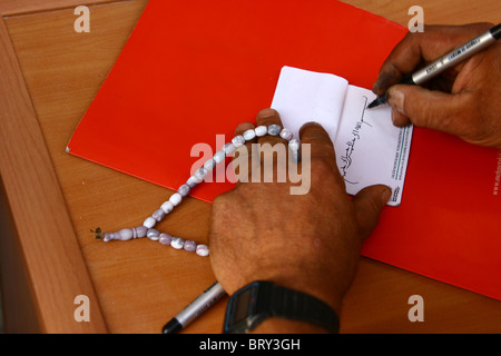 Imam writing God's name in Arabic holding a rosary Stock Photo