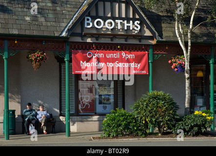 Couple sitting outside Booths supermarket in the town of Keswick, Cumbria, England UK Stock Photo