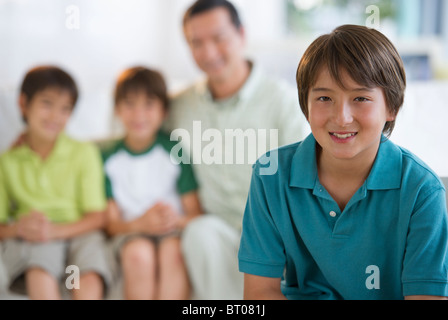 Smiling boy in living room with father and brothers in background Stock Photo