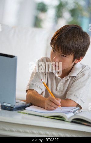 Mixed race boy doing homework and looking at laptop Stock Photo