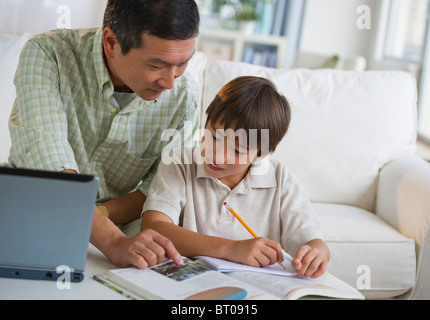 Father helping son with homework in living room Stock Photo