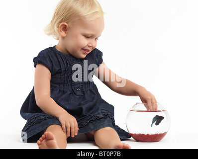 Portrait of a smiling two year old girl playing with a fish in a bowl isolated on white background Stock Photo
