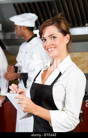 young happy waitress in restaurant kitchen with chefs behind Stock Photo