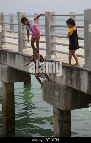 Little girls jumping into the sea from a pier at Rawai, Phuket Thailand Stock Photo