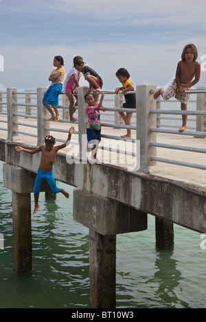 Little girls jumping into the sea from a pier at Rawai, Phuket Thailand Stock Photo