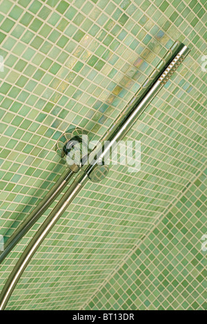 Close-up of stainless-steel shower on green mosaic-tiled wall Stock Photo