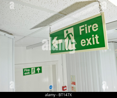 green fire exit sign hanging from ceiling pointing to escape exit Stock Photo