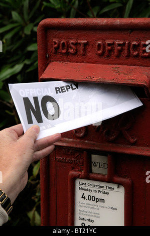 Woman's hand holding and posting a letter containing the words NO Reply into a Post Office posting box Stock Photo