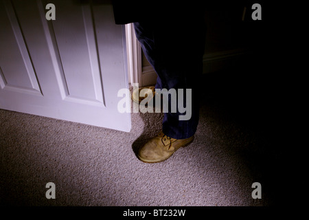 Mens feet with dirty old boots standing by a partially open door Stock Photo