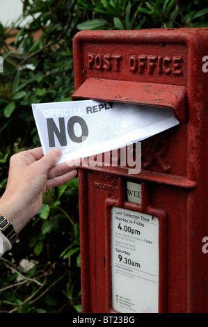 Woman's hand holding and posting a letter containing the words NO Reply into a Post Office letter box Stock Photo