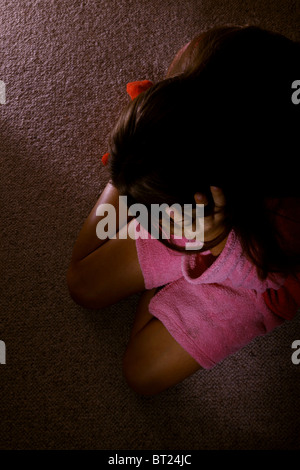 Girl wearing a dressing gown, sitting on a carpeted floor with her head in her hands.