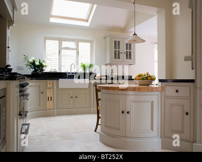 Off-white fitted units in modern kitchen extension with limestone flooring and large sky-light Stock Photo