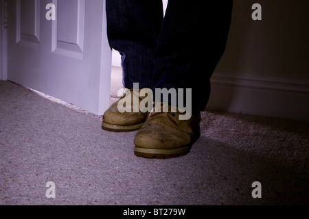 Man wearing old boots standing inside an open door, feet only. Stock Photo