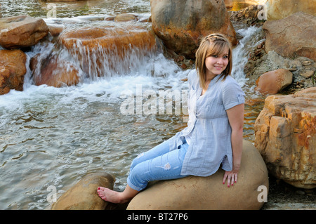 A pretty teen girl poses by a small river on a warm late summer afternoon in warm, golden hour, near sunset light.  By D.Young. Stock Photo