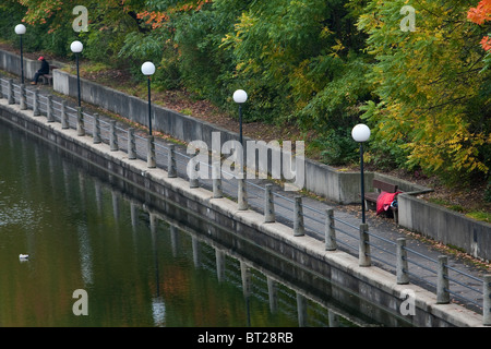 A homeless person sleeps on a bench by the Rideau Canal in Ottawa Stock Photo
