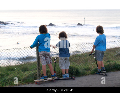 Three young boys watching the surfers, early evening, Bude, Cornwall, UK Stock Photo