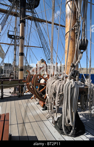 Steering wheel and ropes coiled around belaying pins aboard the Grand Turk, a three-masted frigate at Saint Malo, Brittany Stock Photo