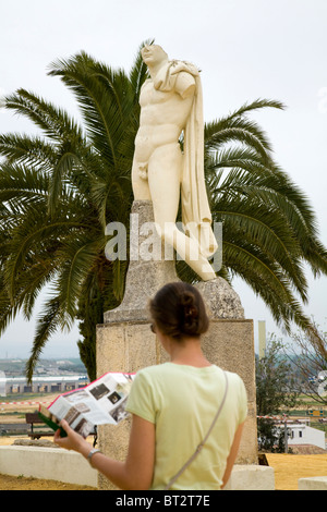 Tourist reads a guide book, & replica of statue of Roman Emperor Trajan in ruined city of Italica / Itálica near Seville, Spain. Stock Photo