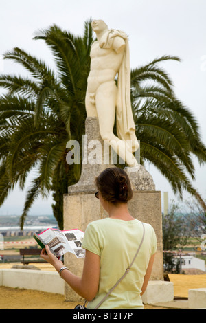 Tourist reads a guide book, & replica of statue of Roman Emperor Trajan in ruined city of Italica / Itálica near Seville, Spain. Stock Photo