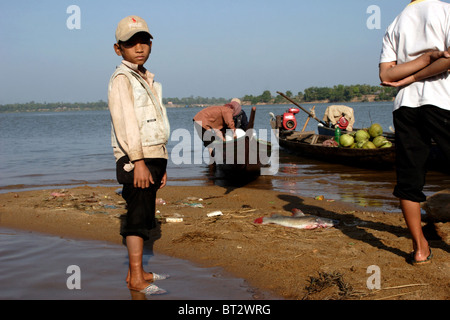 A young Asian boy is standing on the shore of the Mekong River with food supplies at Stung Treng Pier in Stung Treng, Cambodia. Stock Photo