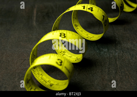 A coiled yellow tape measure against a dark background Stock Photo