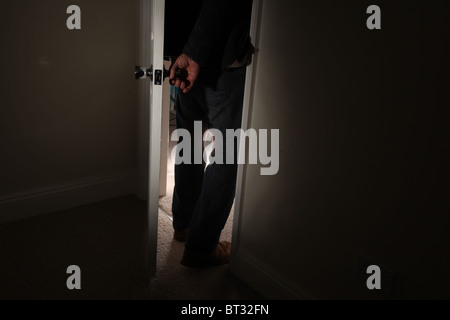 Man turning the handle opening a door entering a dark room Stock Photo