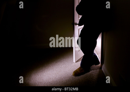 Figure of a man standing in a dark shadowy room arms crossed Stock Photo
