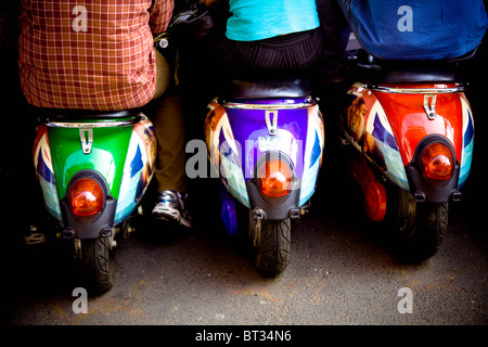 Backs of three people sitting on three brightly colored mopeds Stock Photo