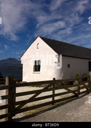 Sunlit white cottage at Ord on the Isle of Skye with a brilliant blue sky, Loch Eishort and Cuillin Mountains behind. Stock Photo