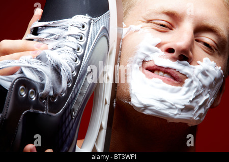 Close-up of handsome man shaving with skate razor on a red background Stock Photo