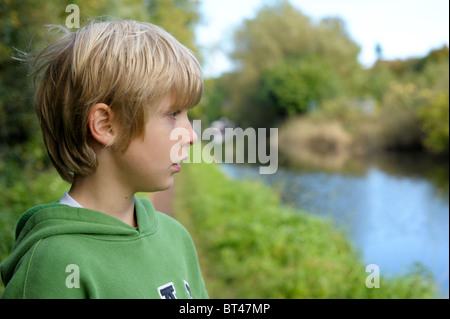 Sad, tired and lonely blond-haired little boy in a green top on his own after being bullied by his mates while out playing Stock Photo