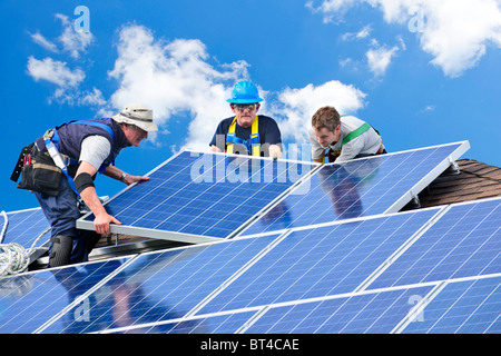 Workers installing alternative energy photovoltaic solar panels on roof Stock Photo
