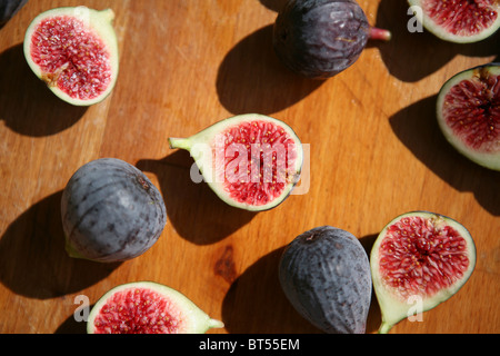 (Ficus carica) Halved and whole fresh figs on a wooden chopping board, sunshine. Stock Photo