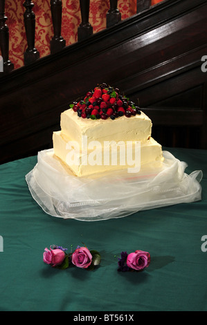 A cream coloured two tiered wedding cake with fresh summer fruits on the top and three roses, button hole flowers. May 2010 Stock Photo