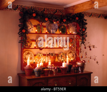 Christmas garland on shelves above sideboard with lighted candles in old terracotta flower-pots Stock Photo